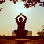 Silhouette of a person practicing yoga outdoors during sunrise, creating a calming atmosphere.