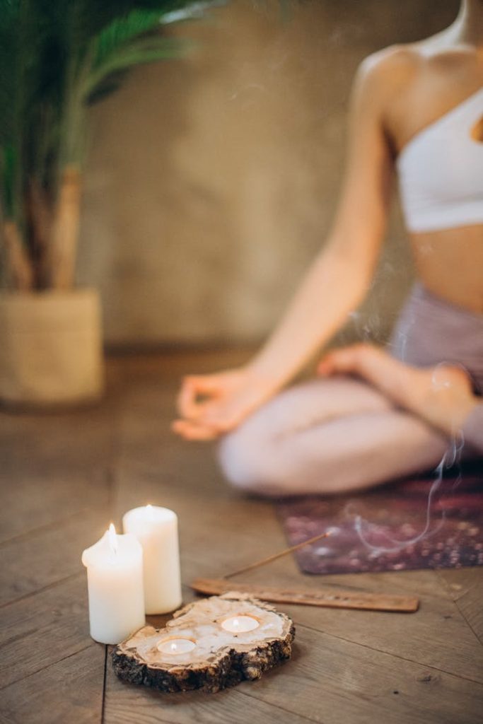 pexels-photo-3822622 Woman practicing meditation in lotus pose with candles and incense, focusing on wellness and relaxation.
