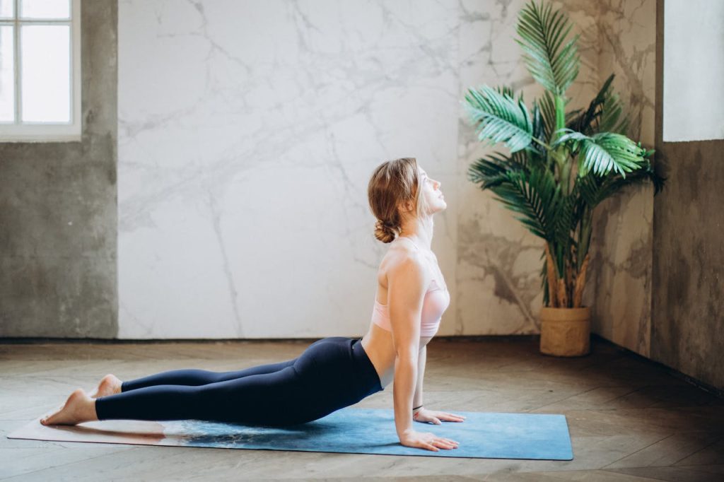 pexels-photo-3823076 Woman in yoga pose on mat, exercising indoors with natural light and plant decor.
